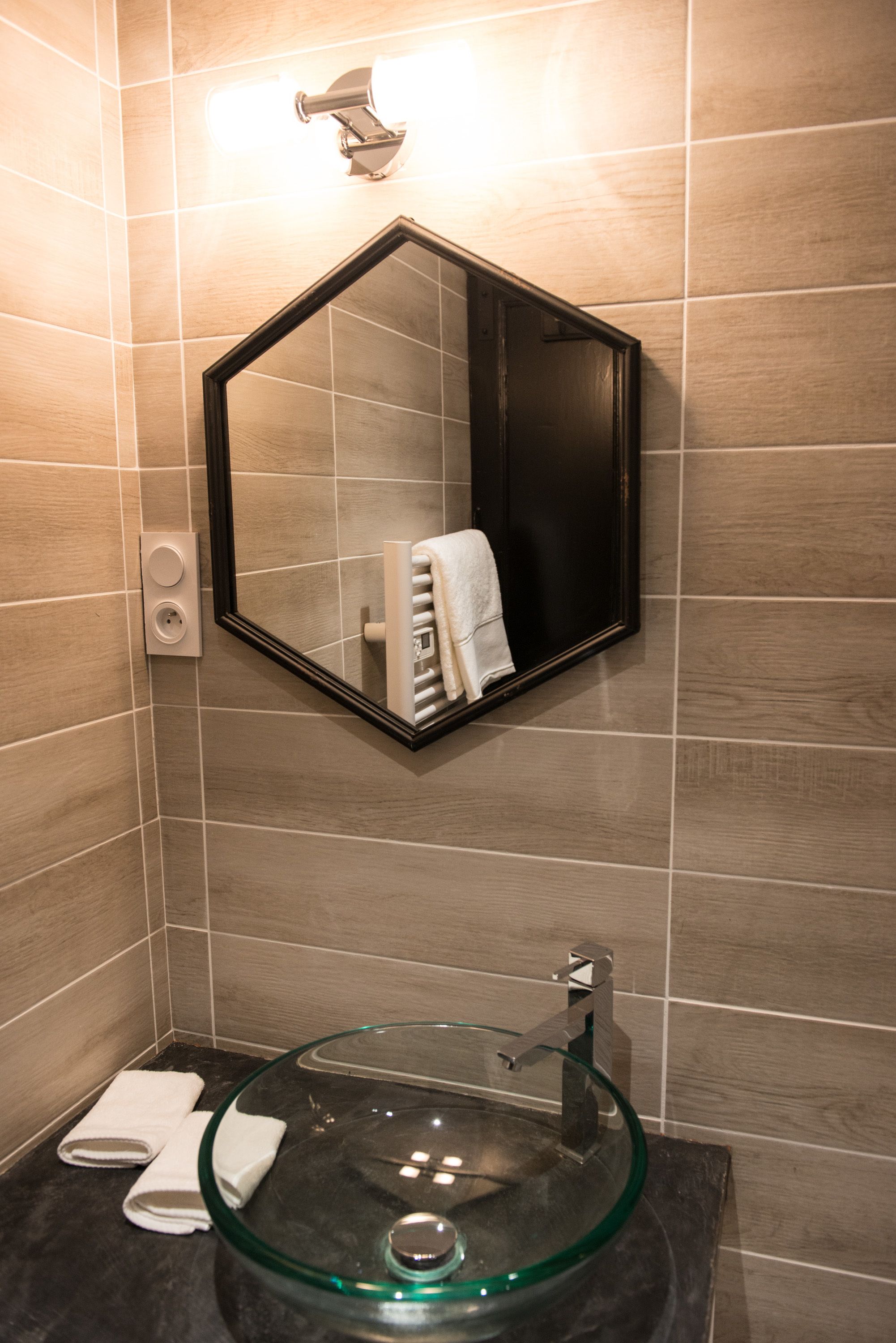 Un baño con un lavabo de cristal, un espejo y un perchero para toallas.