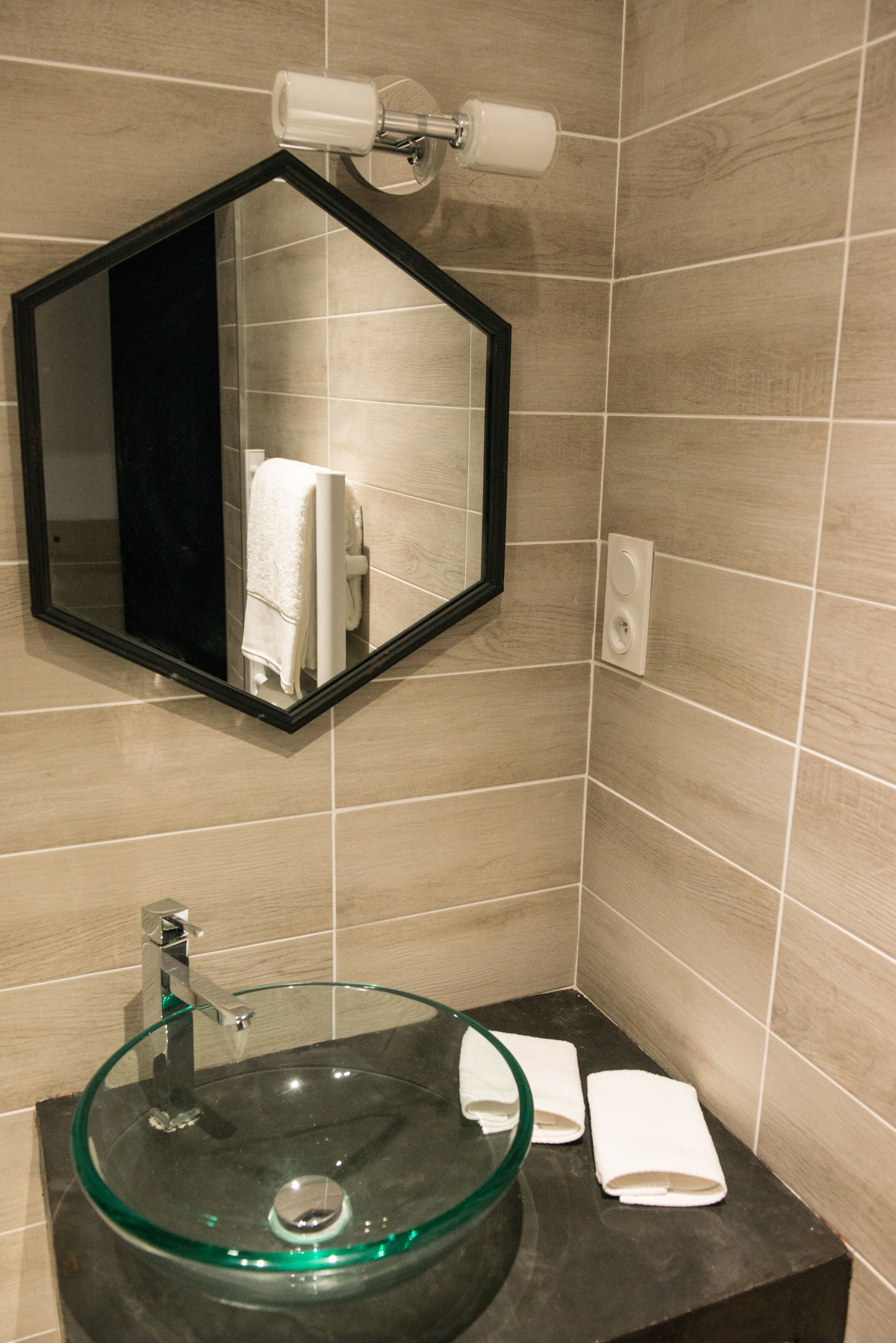 Un baño con un lavabo de cristal, un espejo con marco negro y un perchero para toallas.