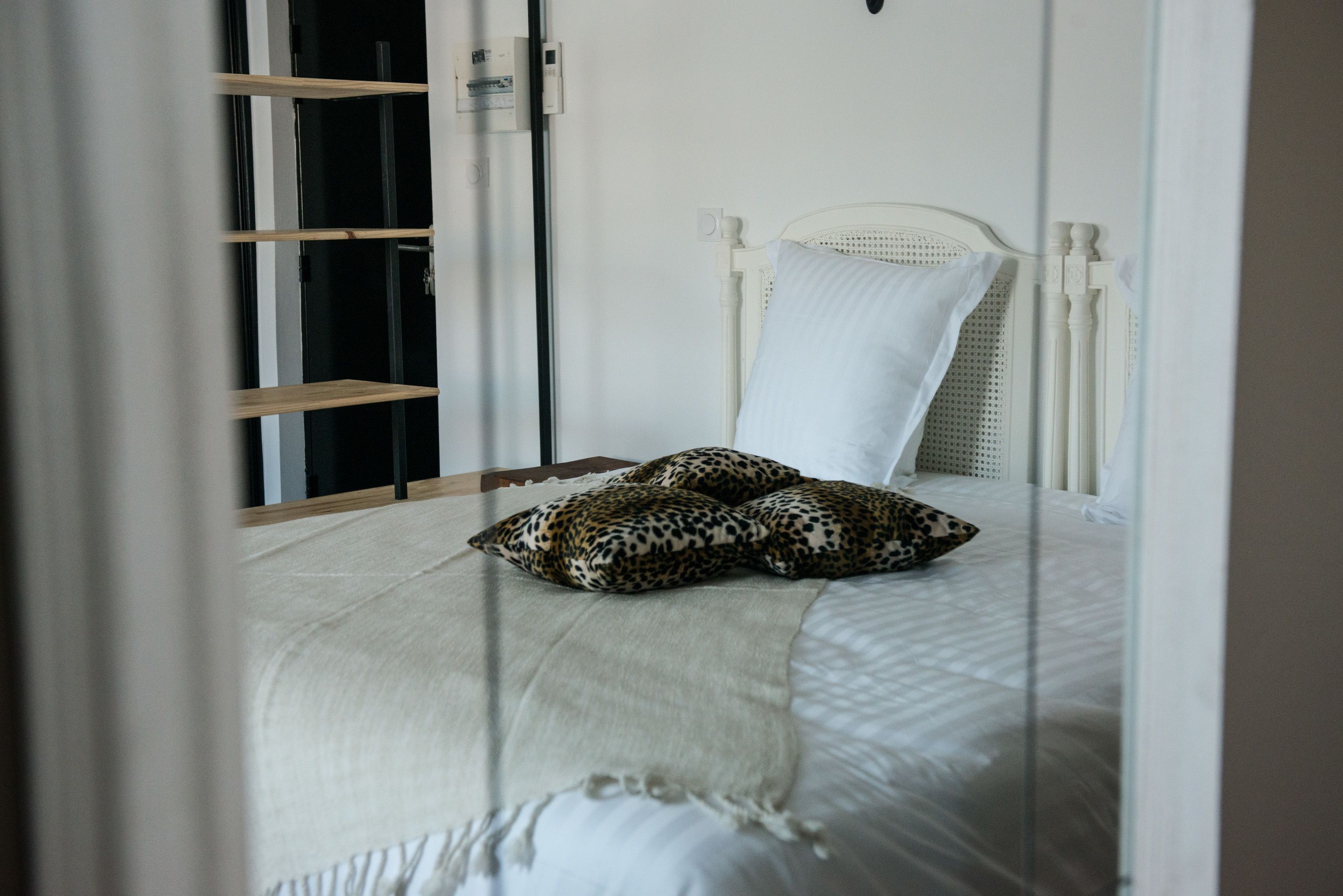 Uma cama com cabeceira e travesseiro brancos, um travesseiro com estampa de leopardo e um cobertor branco.