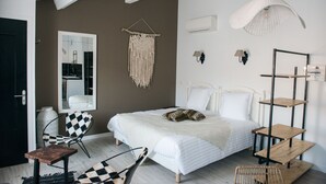 Een slaapkamer met een bed, een stoel, een macramé wanddecoratie, een plank en een hanglamp.