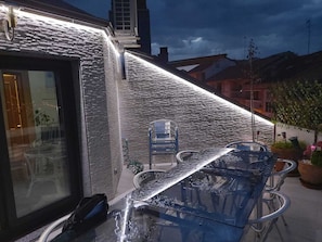Un espace patio avec une table et des chaises en verre, un mur en briques et une fenêtre donnant sur la rue.