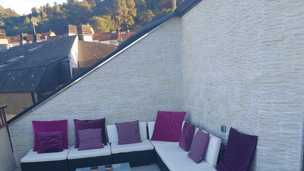 Terraza en la azotea con un sofá modular y una mesa de centro, rodeada por un muro de ladrillo blanco.