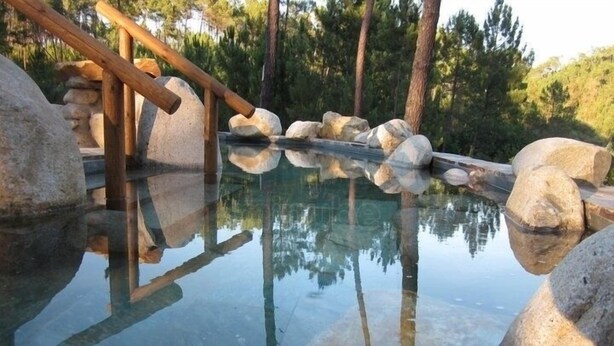 Une piscine aux eaux limpides, entourée de gros rochers et bordée de rampes en bois.