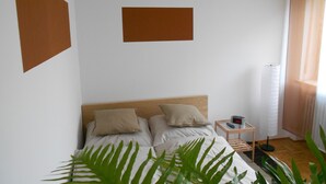 A bedroom with a bed, two pillows, a nightstand with a lamp, and a wall clock. - Hofgarten (Regensburg)