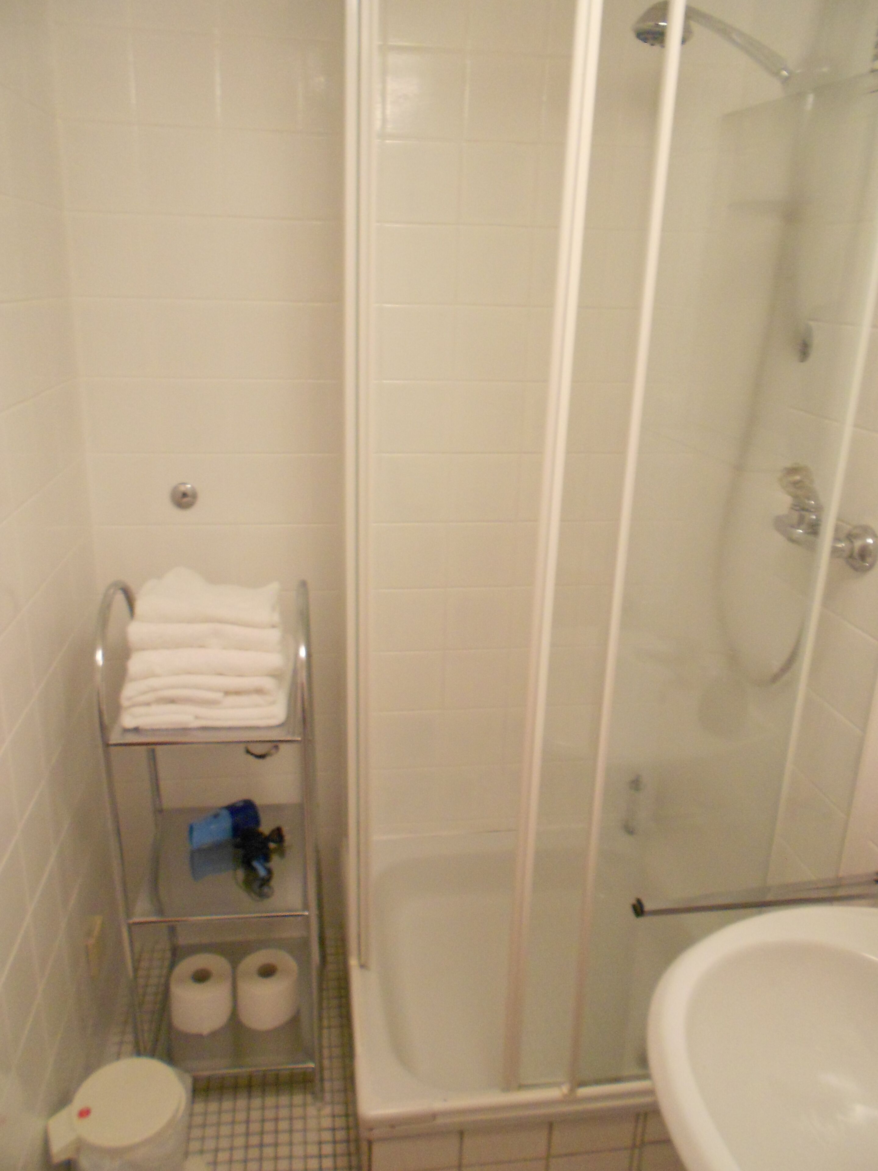 A bathroom with a glass-enclosed shower, a sink, and a shelf with towels and toiletries.