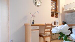 A kitchen with a wooden cabinet, a chair, and a potted plant with flowers. - Hofgarten (Regensburg)
