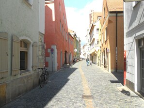 A narrow cobblestone street lined with historic buildings, a bicycle parked on the left, and a pedestrian walking down the path. - Altstadtflair (Regensburg)