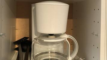 A white coffee maker with a transparent water reservoir and a cup holder on a shelf.