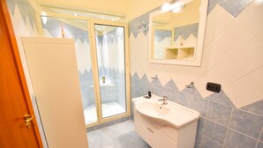 A bathroom with a glass shower enclosure, a sink with a mirror above it, and a cabinet with drawers. - B&B Mary Flower (Naples)