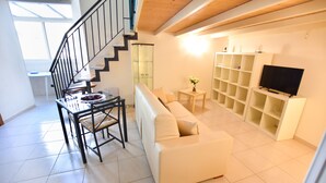 A living room with a staircase, a sofa, a TV, and shelves. - B&B Mary Flower (Naples)