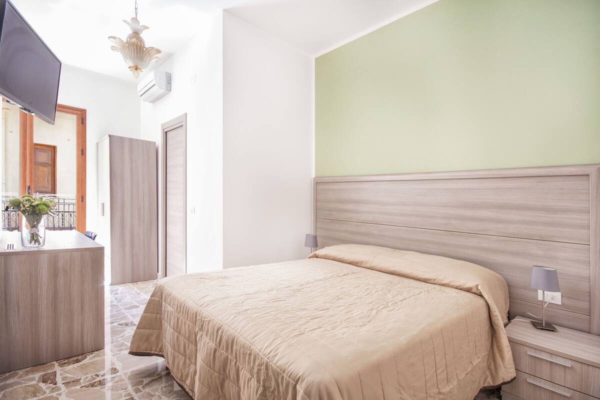 Une chambre à coucher avec un lit, des tables de chevet, un téléviseur et une salle de bain visible à travers une porte ouverte.