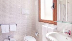 Une salle de bain équipée d’un bidet, de toilettes et d’un lavabo, avec des murs carrelés et un grand miroir.