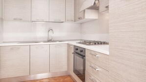 Une cuisine moderne avec des meubles blancs, une cuisinière à gaz et un évier en acier inoxydable.