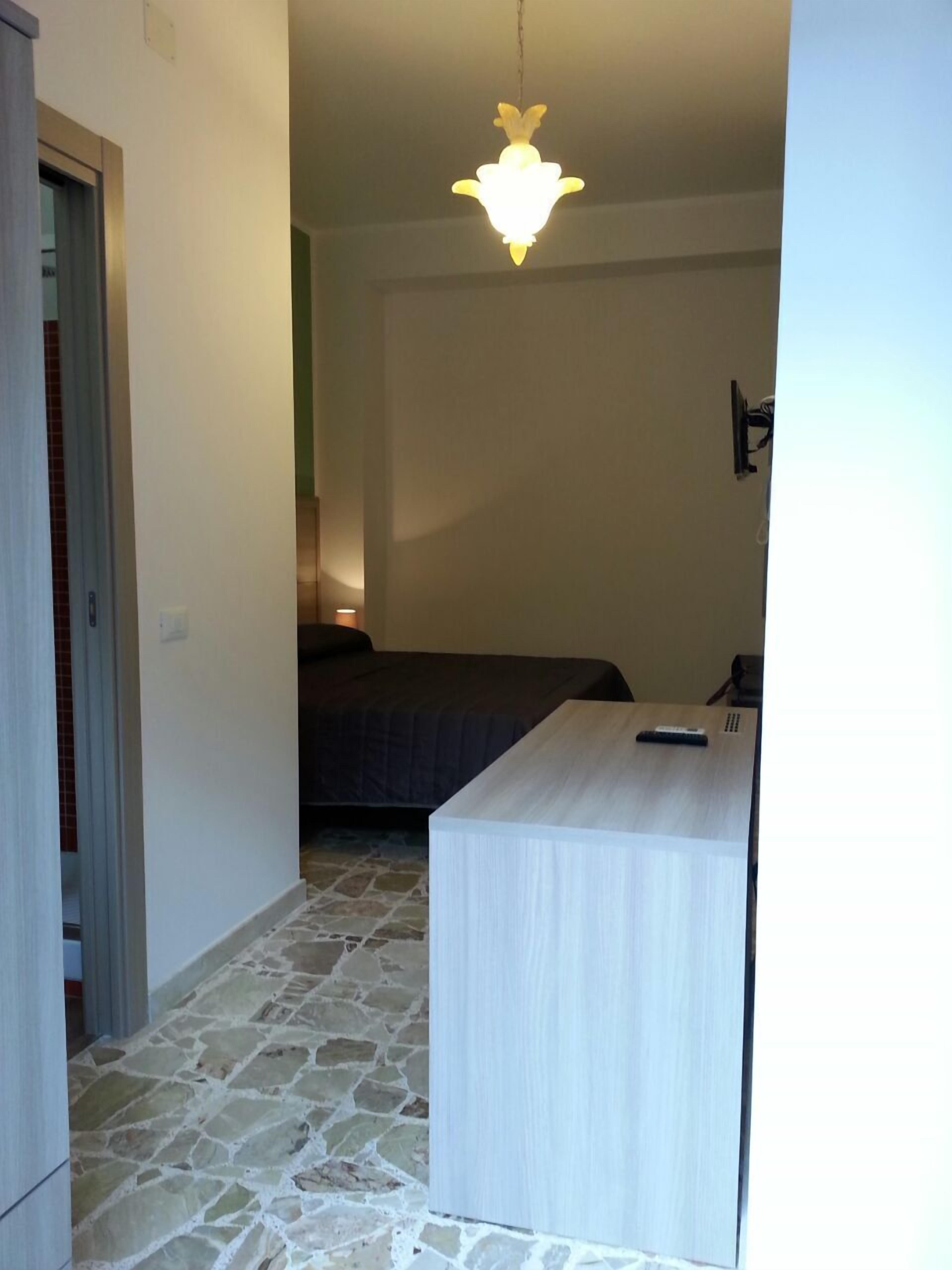 A room with a stone floor, a bed, a desk, and a hanging light fixture.