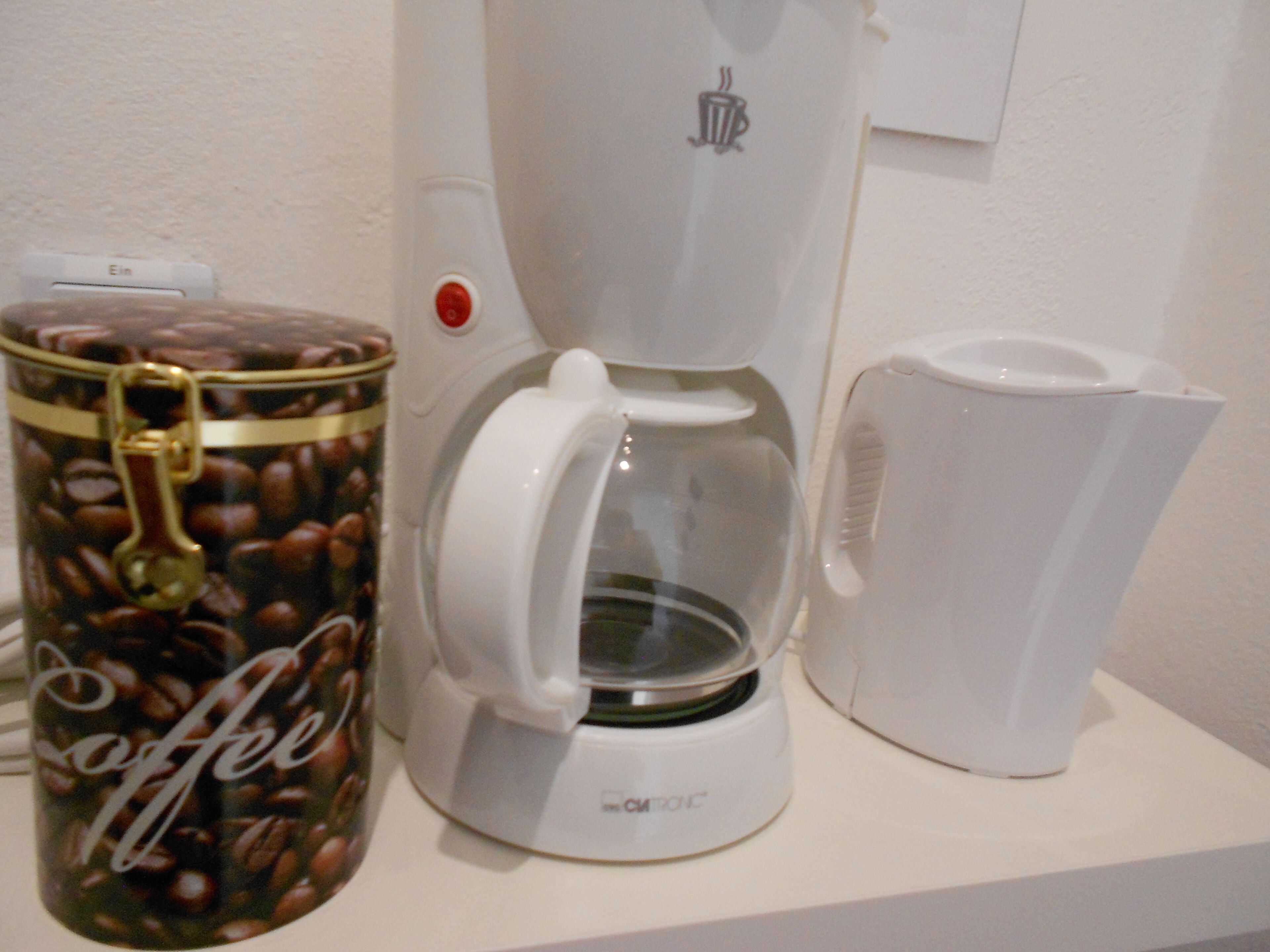 En kaffemaskine, en kaffekande og en beholder med kaffebønner på en hvid bordplade.