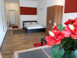 A modern bedroom with a wooden floor, a bed with white bedding, a wooden wardrobe, and a red flower arrangement. - Beethoven (Regensburg)