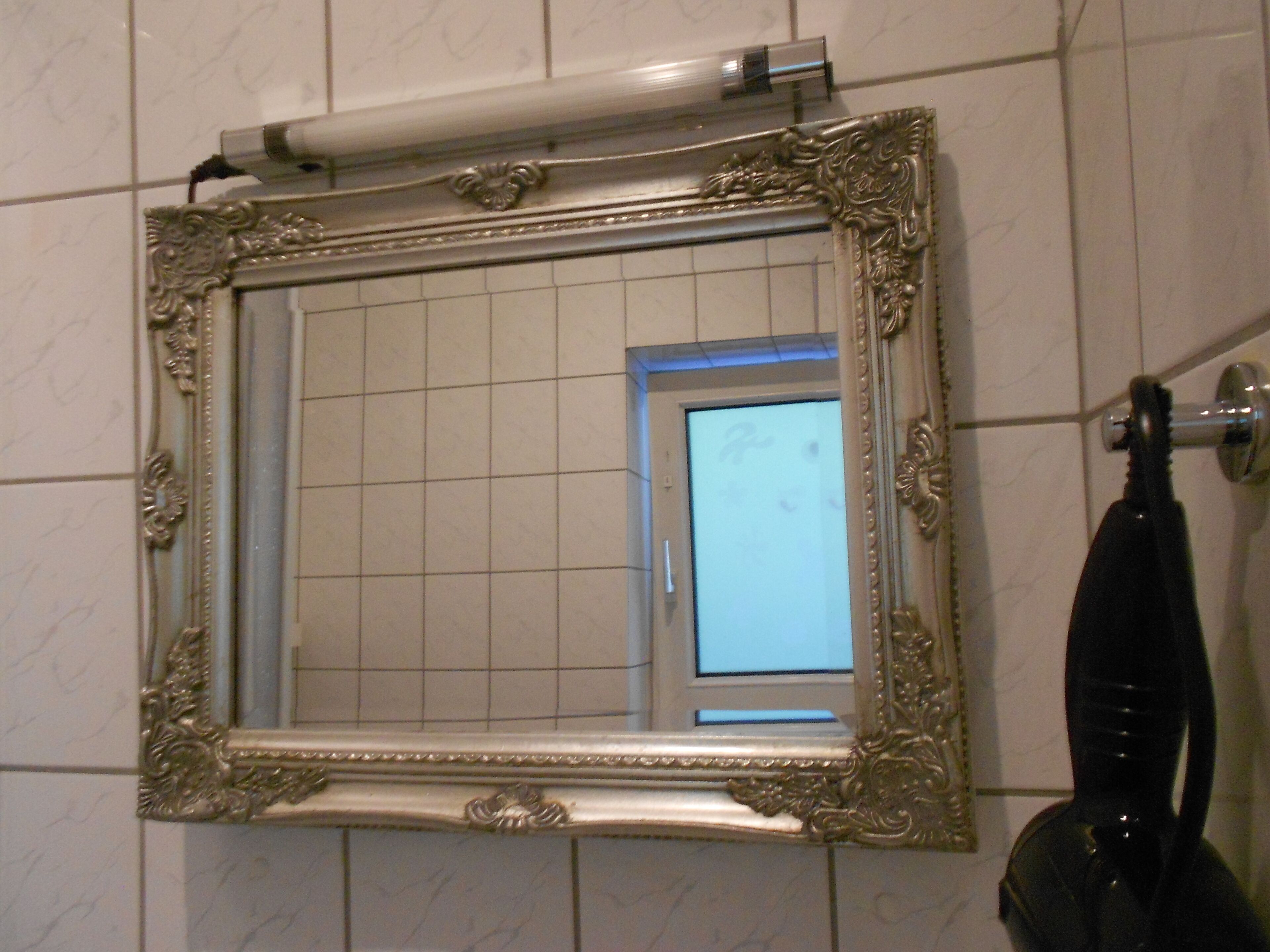 A bathroom with a large ornate mirror, tiled walls, and a visible door.