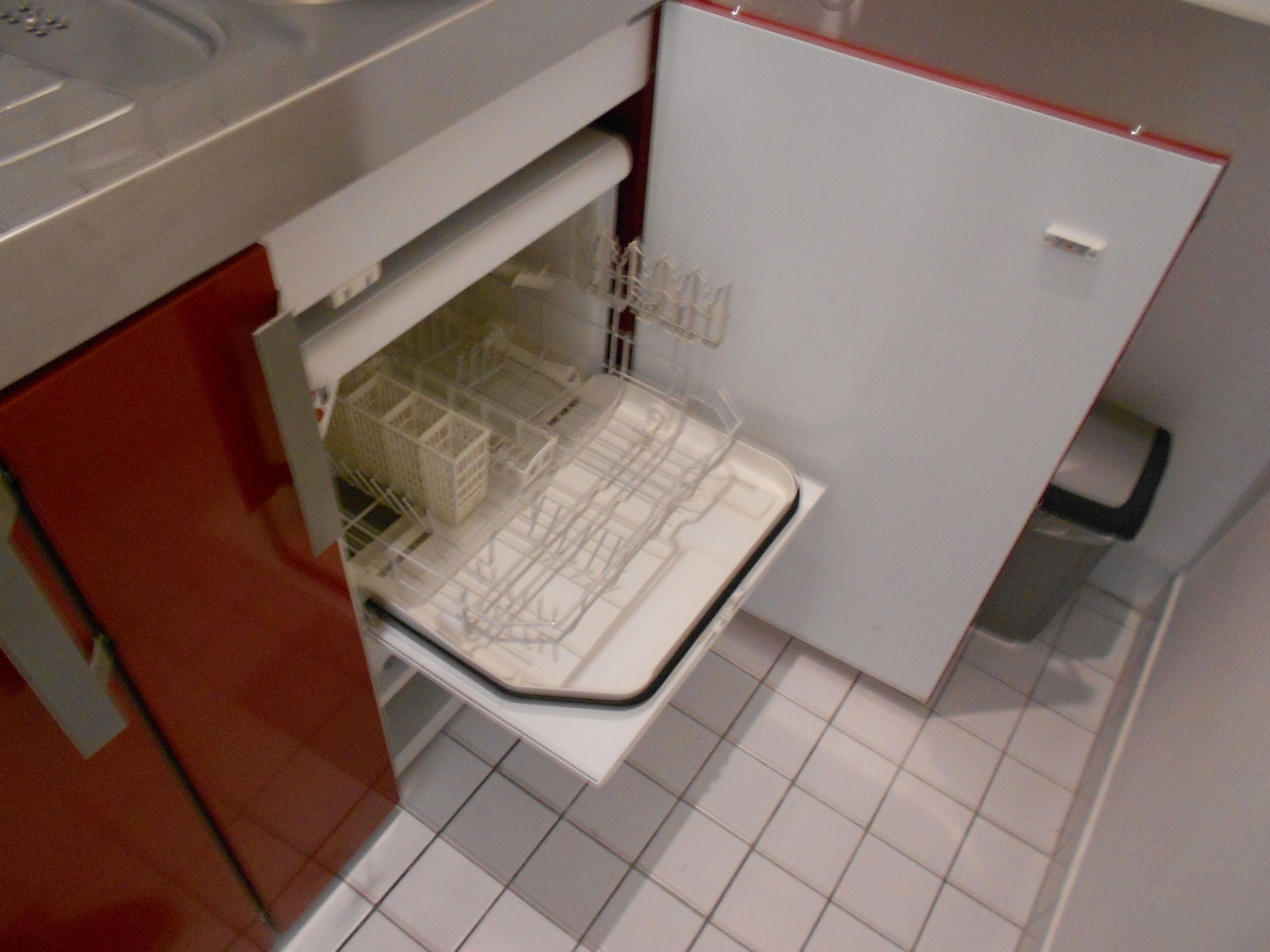 A compact kitchen with a built-in dishwasher, a red cabinet, and a tiled floor.