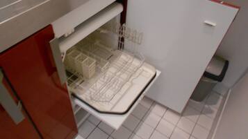 A compact kitchen with a built-in dishwasher, a red cabinet, and a tiled floor.