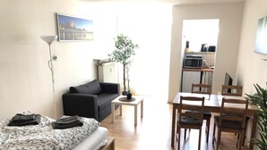 A compact living space with a bed, a sofa, a dining table with chairs, a small kitchen area, and a potted plant. - Newstyle (Regensburg)