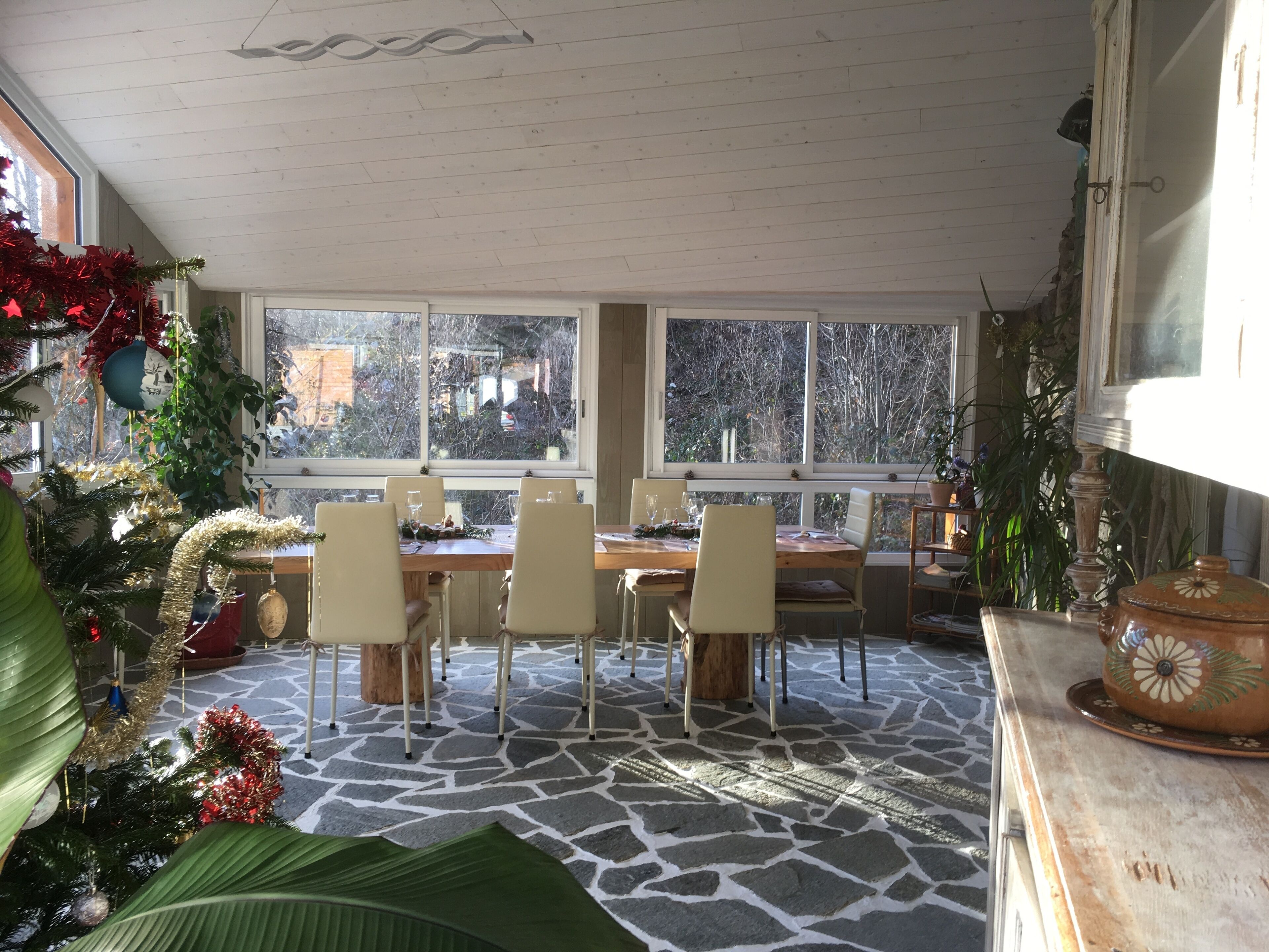Un comedor con una mesa dispuesta para cuatro personas, rodeada de sillas, ventanas amplias y un piso con diseño de piedra.