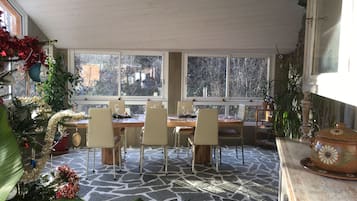 Un comedor con una mesa dispuesta para cuatro personas, rodeada de sillas, ventanas amplias y un piso con diseño de piedra.