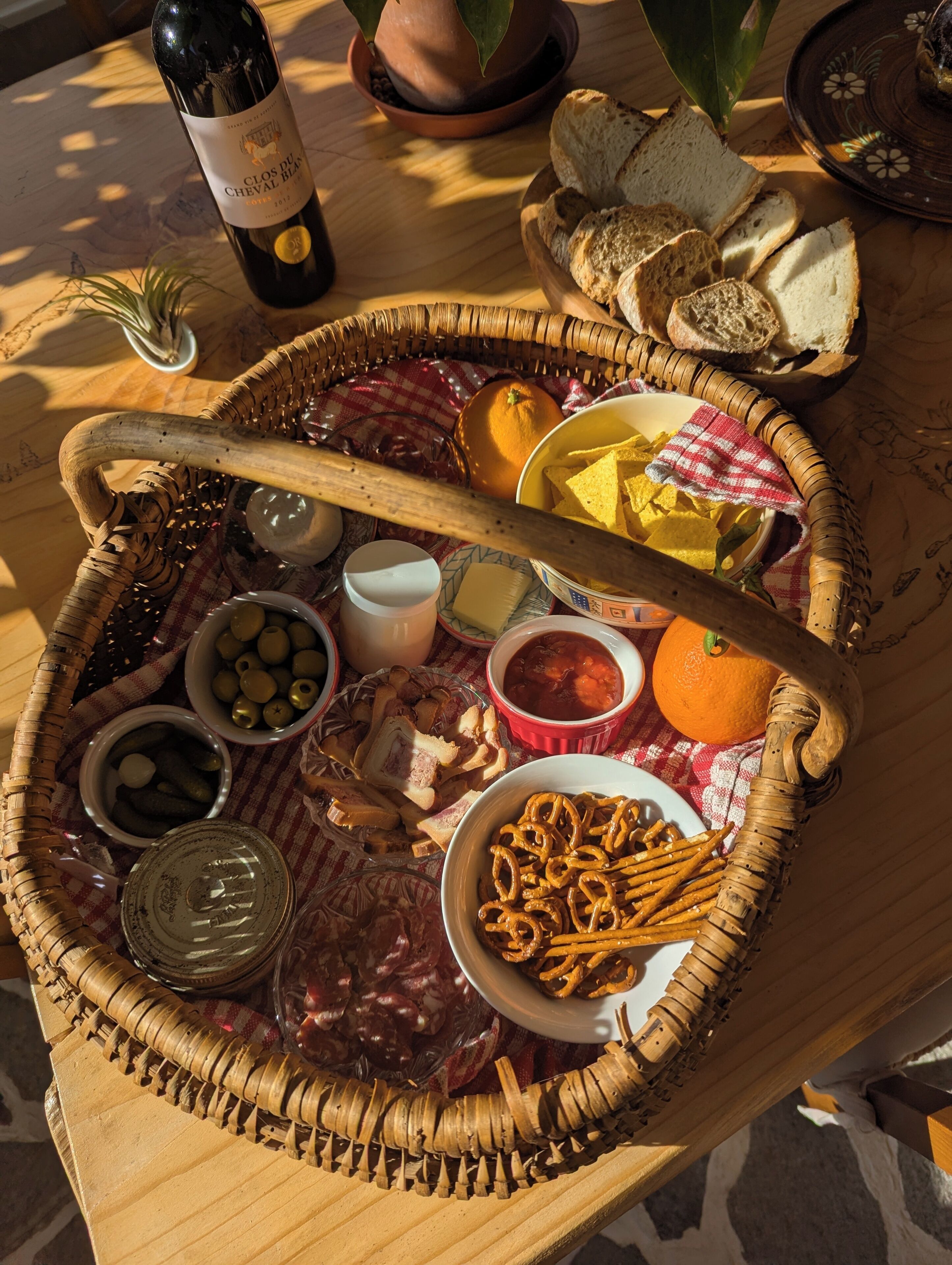 Una cesta de mimbre llena de diversos alimentos y una botella de vino sobre una mesa de madera.