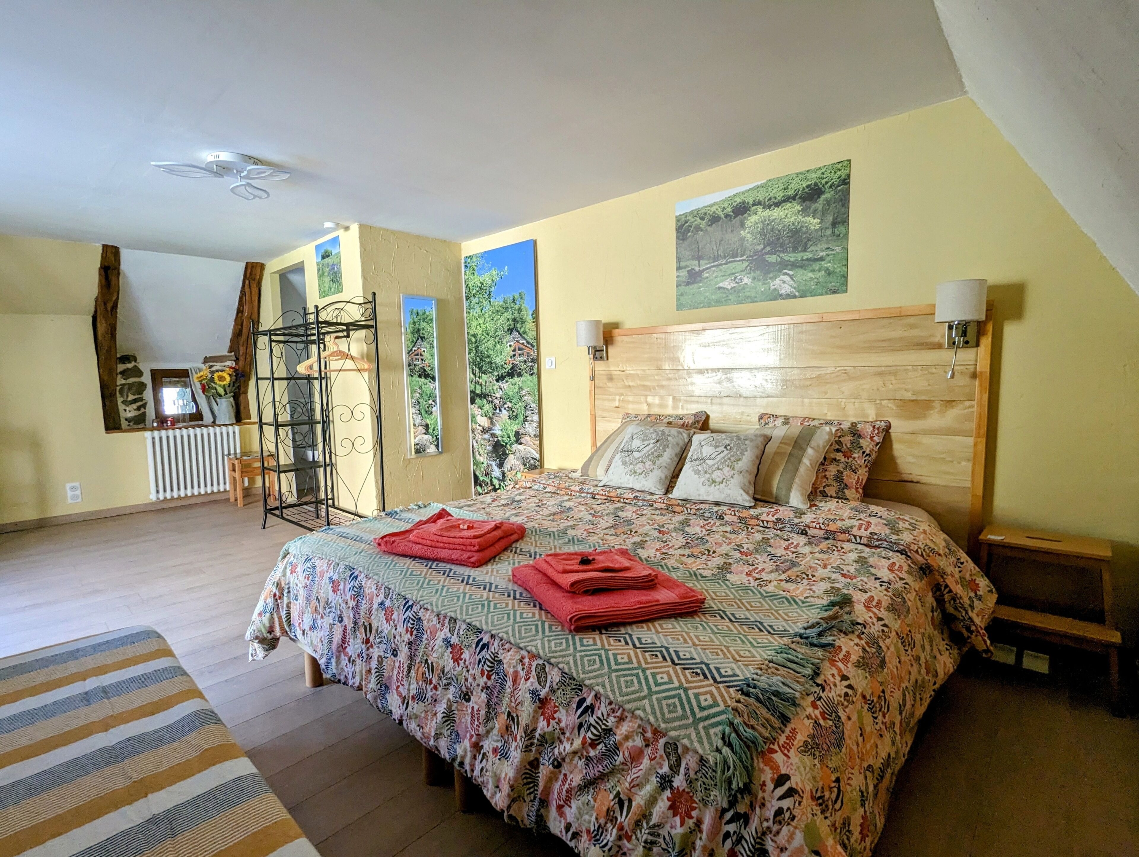 Une chambre à coucher avec une tête de lit en bois, une couvre-lit à motifs et une vue sur un paysage verdoyant par la fenêtre.
