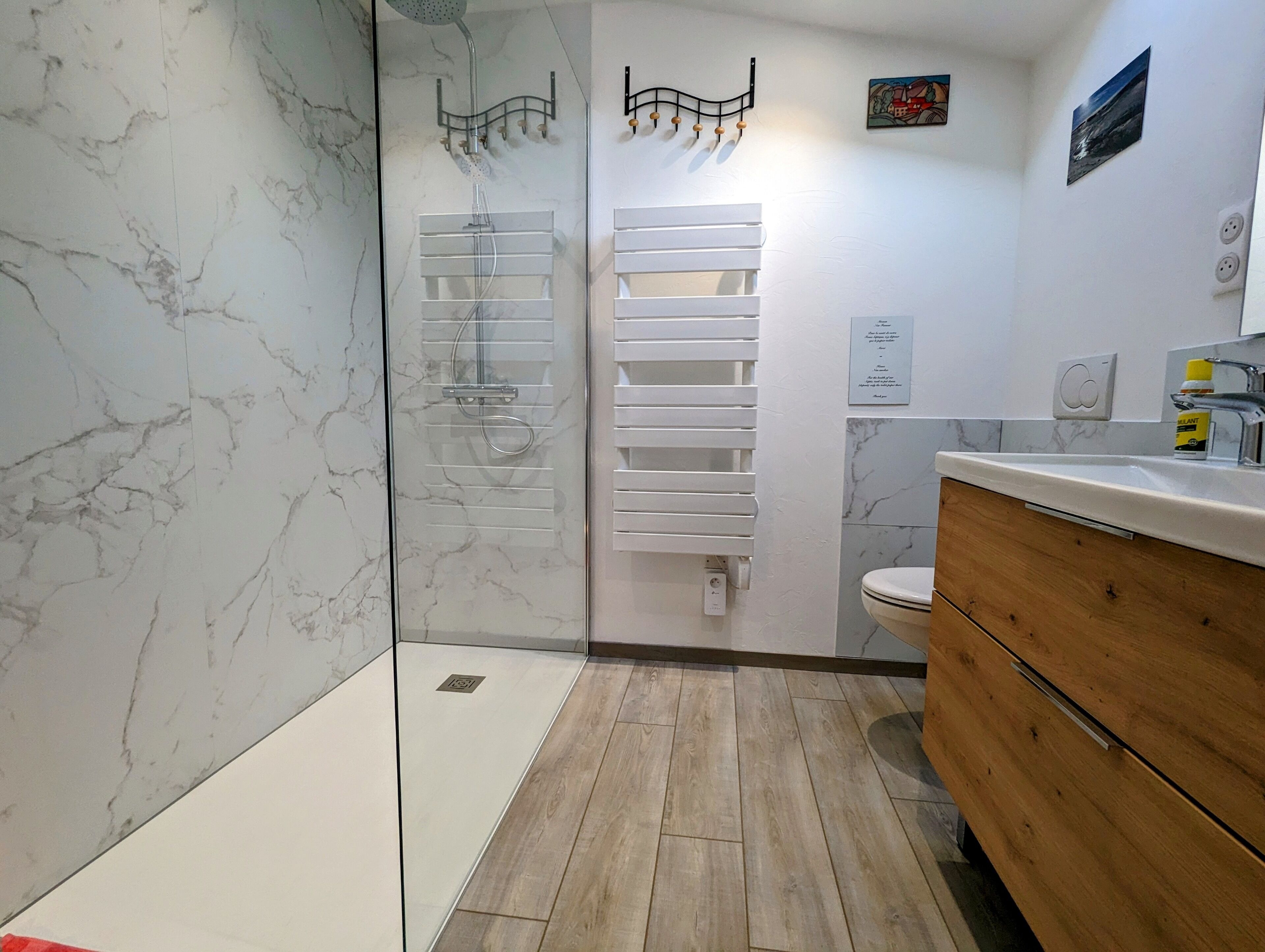 Une salle de bain moderne avec une douche à l’italienne en verre, un meuble-lavabo en bois et un pare-baignoire en marbre.