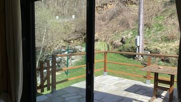 Een balkon met een stenen vloer, een houten tafel en uitzicht op een natuurlandschap met bomen en een heuvel.
