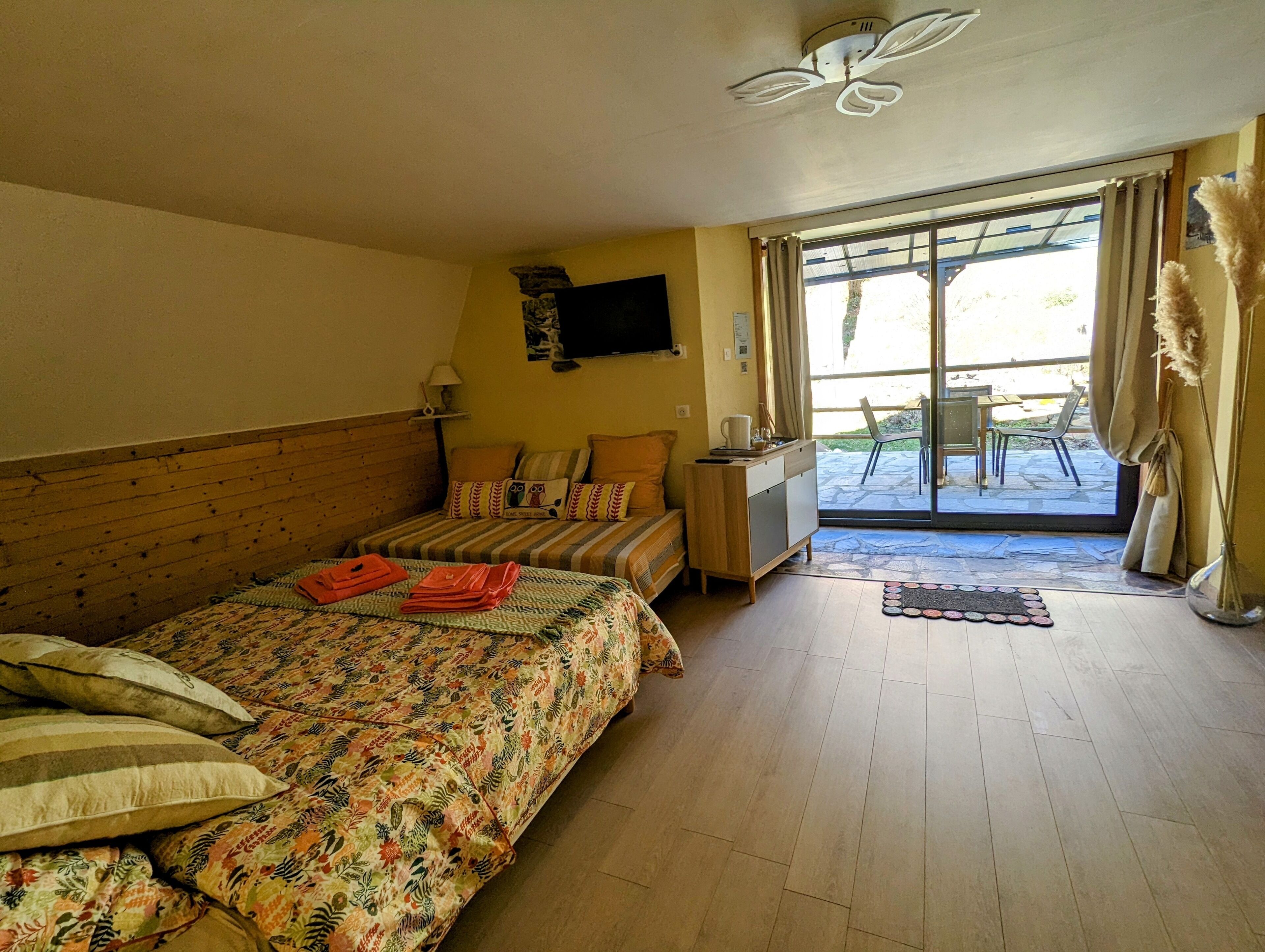 Un dormitorio con cama, cabecera de madera, televisor montado en la pared y puerta corrediza de vidrio que da a un área exterior.