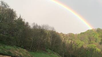 A rural landscape with a rainbow, a wooden shed, and a grassy hill.