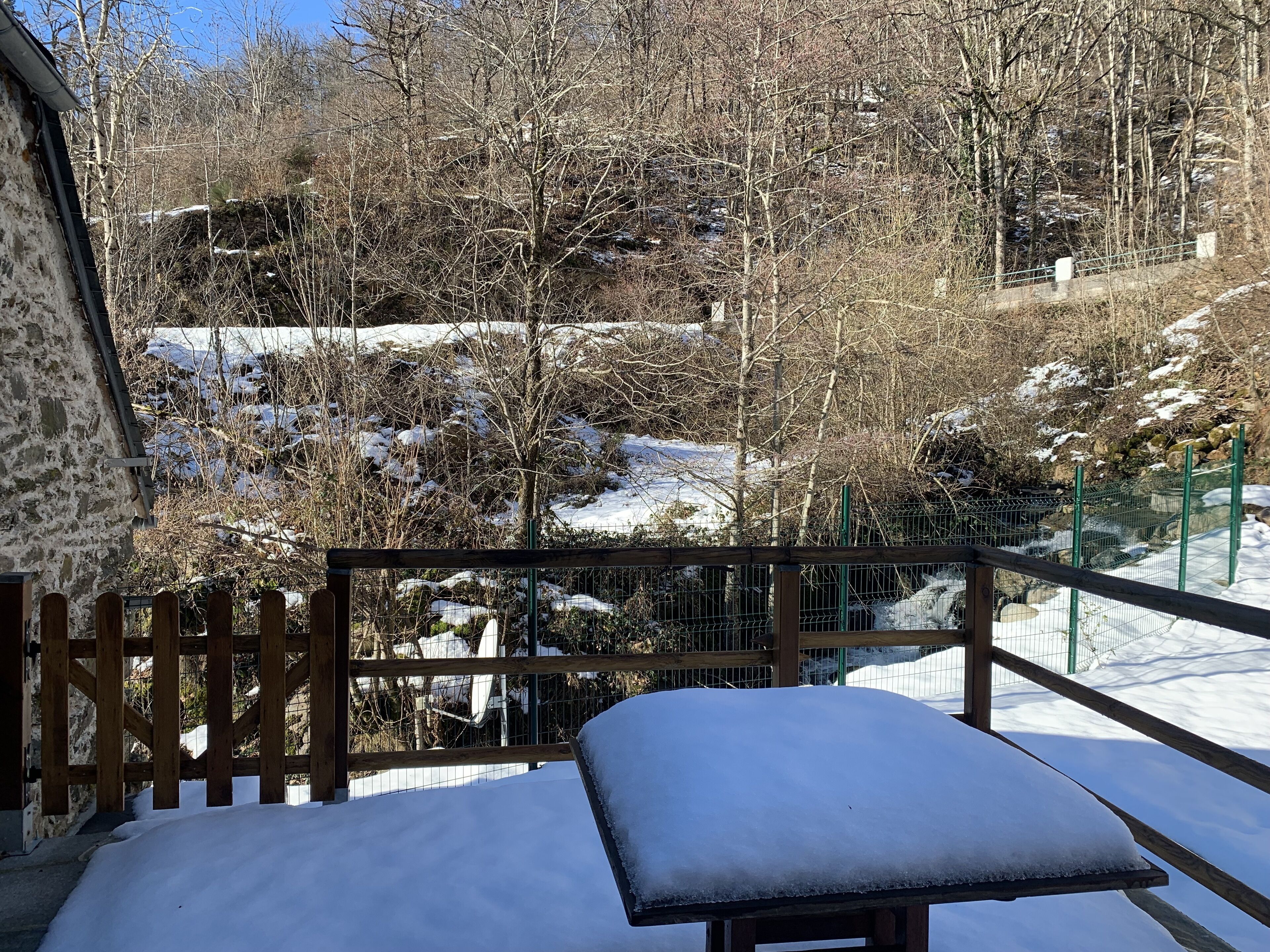 A snow-covered outdoor area with a wooden bench and a stone wall.