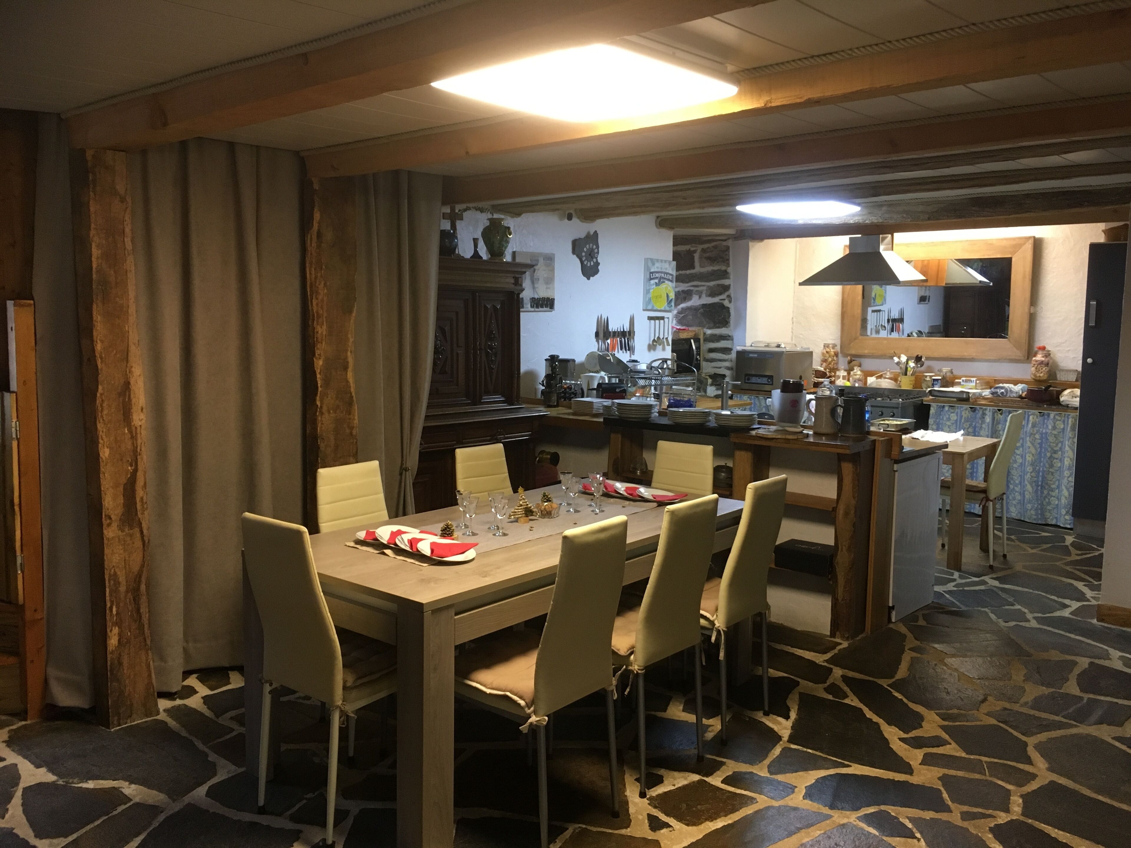A dining area with a stone-tiled floor, a wooden table set for six, and a kitchen in the background.