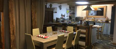 A dining area with a stone-tiled floor, a wooden table set for six, and a kitchen in the background.