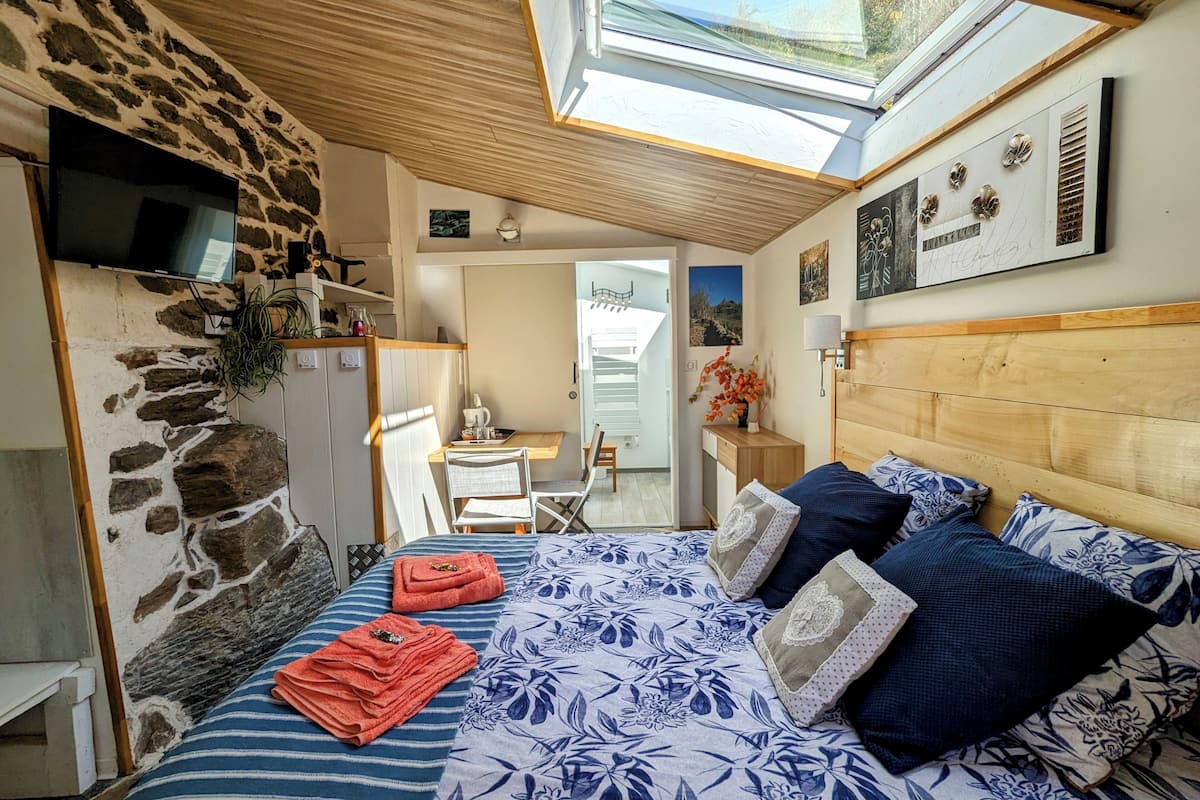 A bedroom with a stone wall, a bed with blue floral bedding, a wooden headboard, and a skylight.