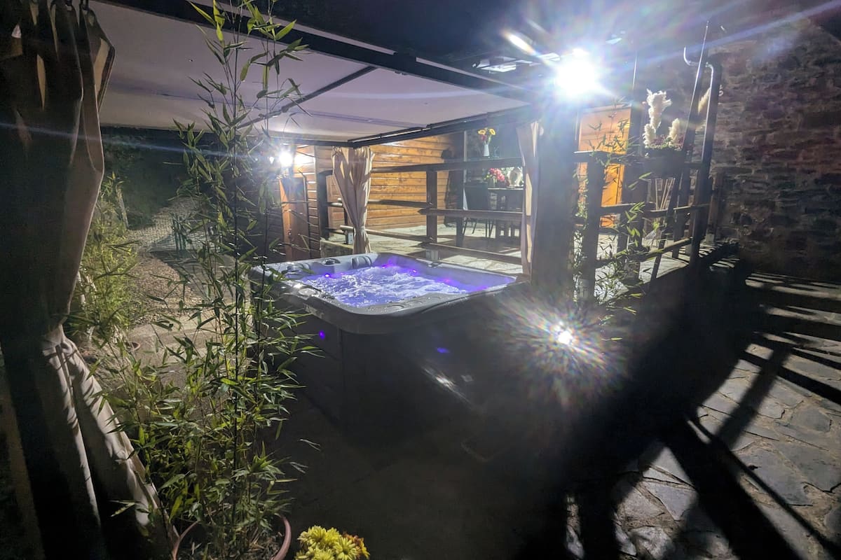 A hot tub in a covered outdoor area with bamboo plants and a stone wall.