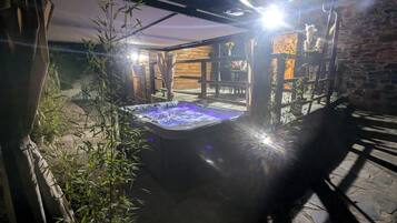 Un jacuzzi en un espacio exterior cubierto con plantas de bambú y una pared de piedra.