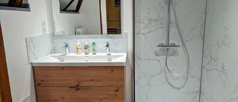 Un baño con tocador de madera, un espejo grande, ducha con pared de mármol y un ventanal pequeño.