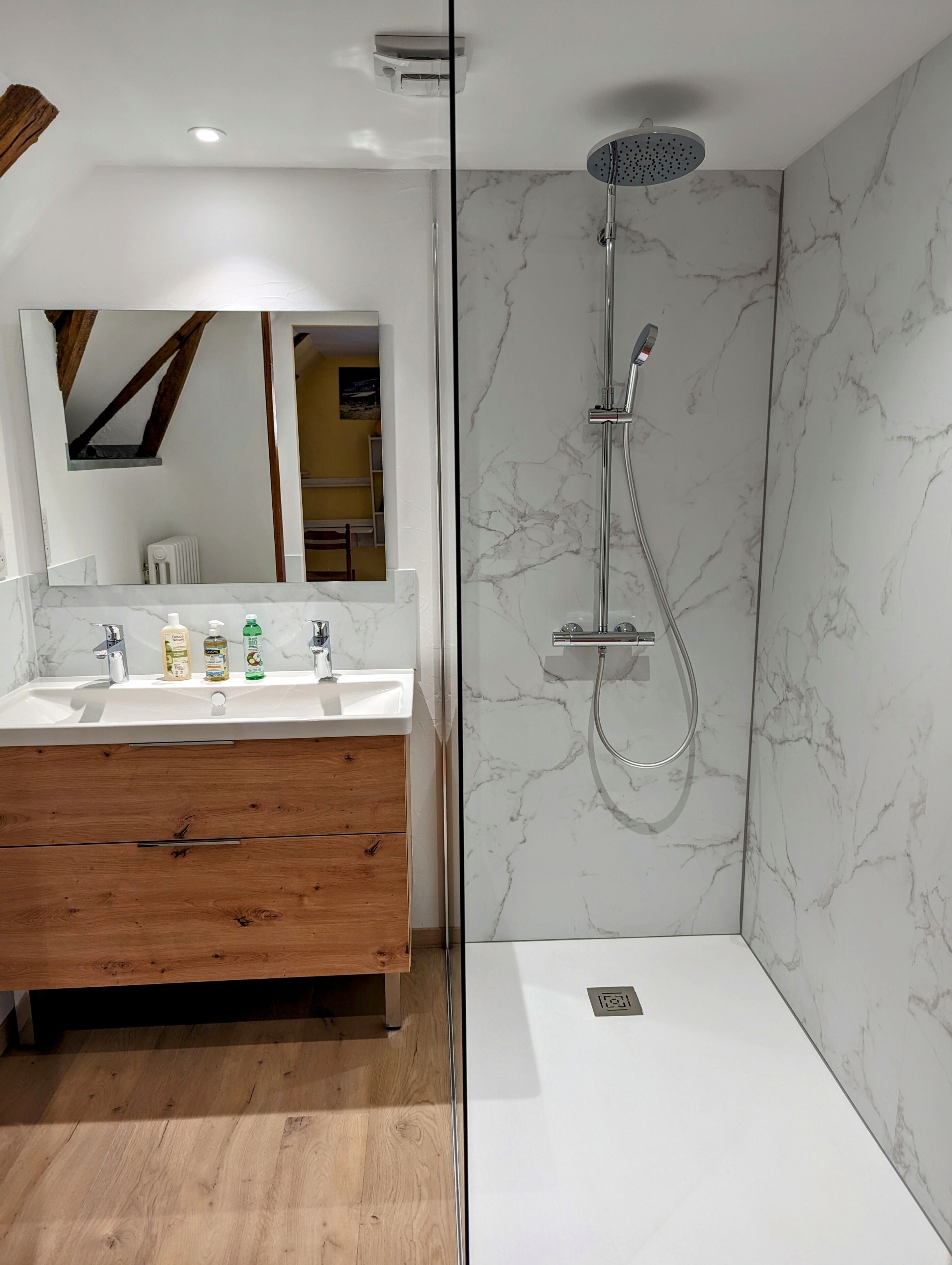 Un baño moderno con ducha de mármol, tocador de madera y un espejo grande.