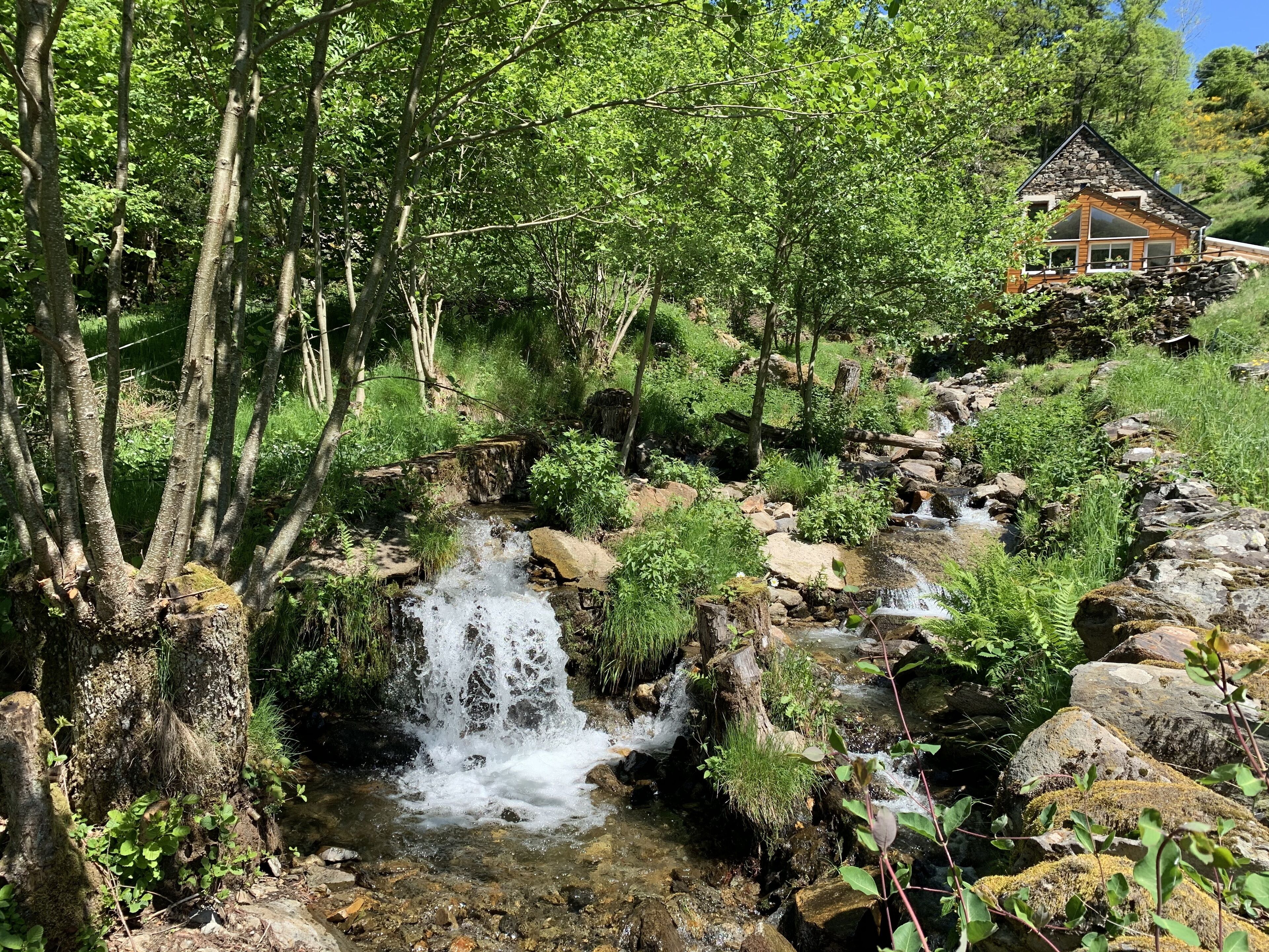 A waterfall in a forested area with a rustic house in the background.