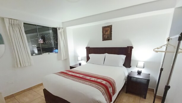 Habitación de hotel con una cama grande, una mesita de noche, una lámpara, una ventana con cortinas y un perchero.
