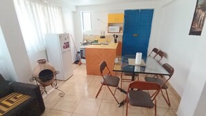 Un espacio habitable compacto con kitchenette, una zona de comedor con mesa de vidrio y un sofá.