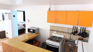 Una cocina compacta con estufa a gas, microondas y armarios color naranja.