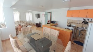 Una sala de estar con un sofá, una mesa de centro y un televisor. Cuenta con una cocina equipada con estufa y fregadero.