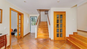 Un pasillo con escaleras de madera, suelo de baldosas y puertas de madera.