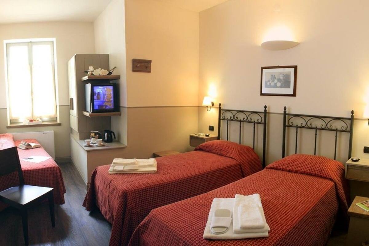 A hotel room with two beds, a desk, a chair, a television, and a window.