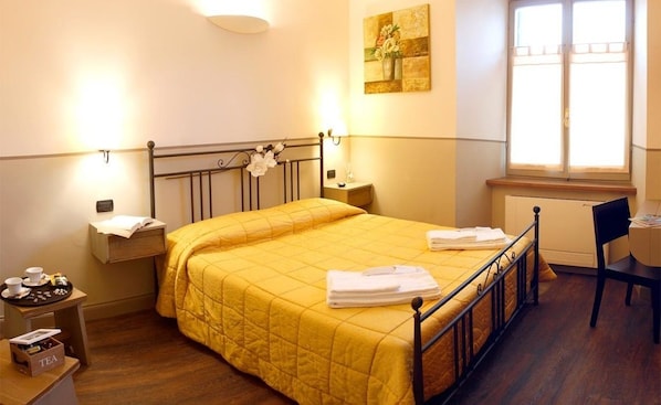 A hotel room with a bed, bedside tables, a chair, a window, and a painting on the wall. - Hotel Da Benito (Norcia)