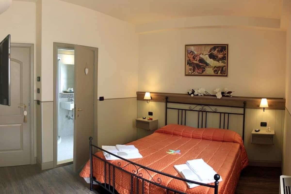 A bedroom with a bed, bedside tables, a painting, and a door leading to a bathroom.