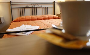 A bed with an orange quilt, a white towel, and a cup on a saucer. - Hotel Da Benito (Norcia)